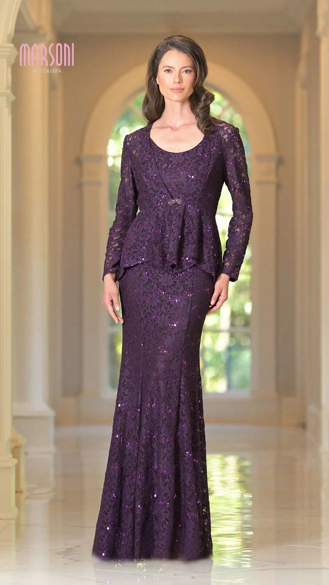 A woman poses indoors in the Marsoni M301 long formal dress, featuring a peplum jacket. The eggplant-colored gown shimmers as she stands before arched windows and columns.